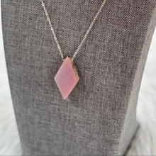 Necklace with a pink pendant on a gray mannequin bust against a blurred natural background