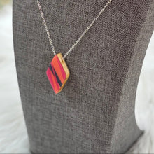Necklace with a red and gold pendant on a gray mannequin bust against a blurred natural background.
