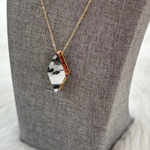 Necklace with a unique pendant on a gray bust against a blurred natural background