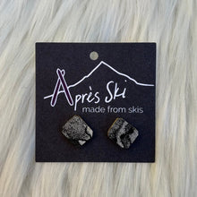 Pair of earrings on a 'Après Ski' branded card against a light wood background