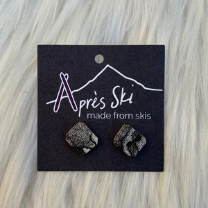 Pair of earrings on a 'Après Ski' branded card against a light wood background