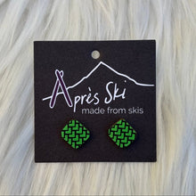 Green patterned earrings on a black card with 'Apres Ski' branding, placed on a wooden surface.