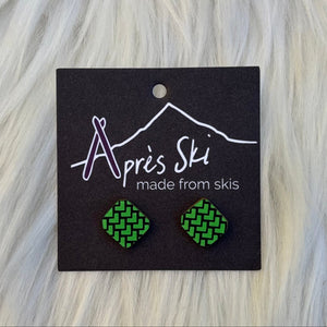 Green patterned earrings on a black card with 'Apres Ski' branding, placed on a wooden surface.