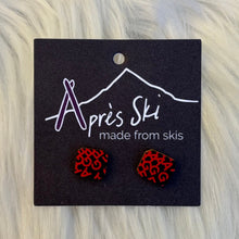 Red patterned earrings on a black card with 'Après Ski' branding against a fur background