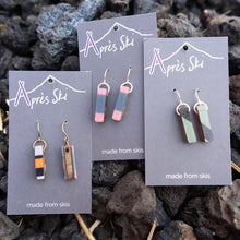 Three pairs of earrings on 'Après Ski' branded cards against a rocky background